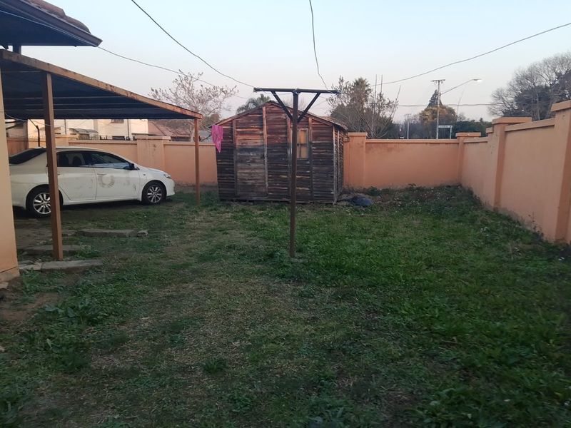 Rear yard area featuring a carport, a wooden storage shed, and a perimeter boundary wall.