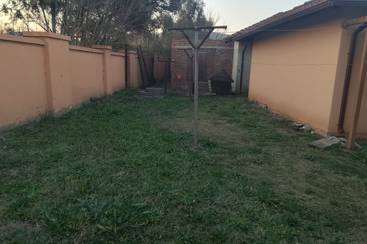 A rear garden area featuring a perimeter wall, a rotary clothesline, and a tiled roof structure, showing signs of wear and maintenance needs.