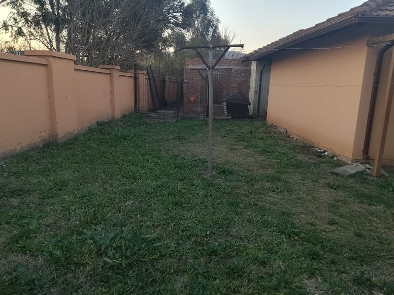 A rear garden area featuring a perimeter wall, a rotary clothesline, and a tiled roof structure, showing signs of wear and maintenance needs.