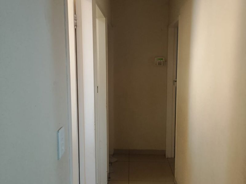 A simple, neutral hallway featuring tiled flooring, a security alarm keypad, and ceiling access, providing a clean and functional transition space.