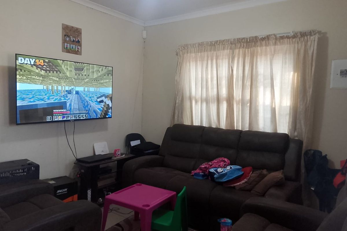 A functional living room featuring neutral wall finishes, cove cornicing, and a window fitted with a curtain rail.