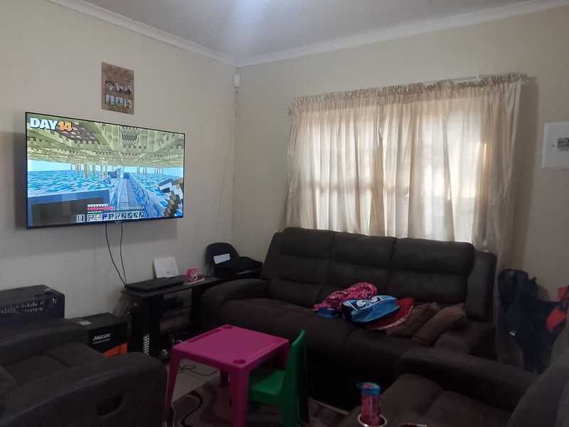 A functional living room featuring neutral wall finishes, cove cornicing, and a window fitted with a curtain rail.