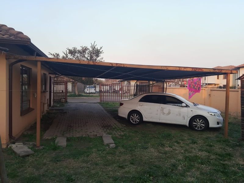 Front exterior view featuring a paved driveway and a metal carport structure with visible signs of weathering and rust.
