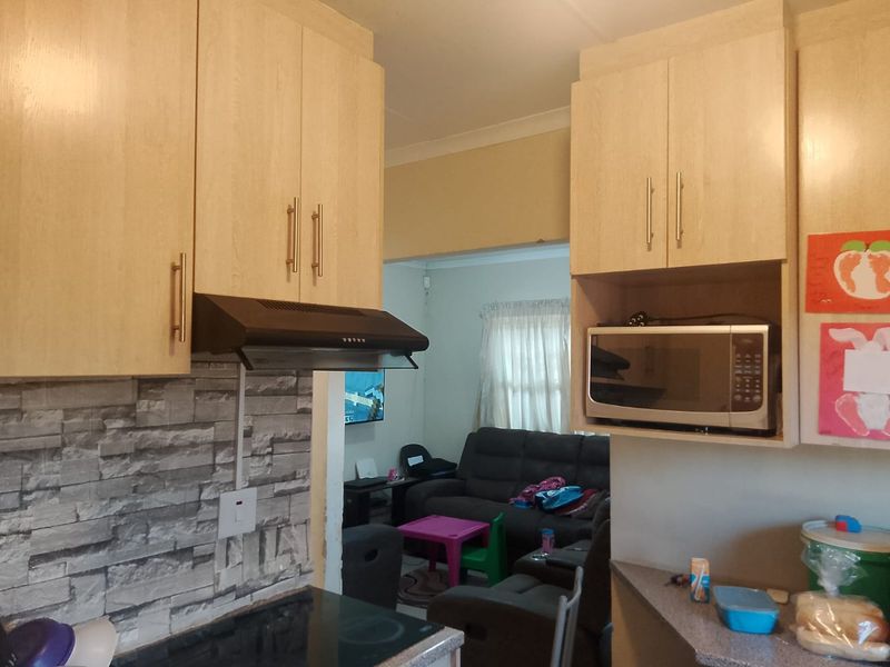 Open plan kitchen featuring light wood cabinetry, stone-look splashback, and integrated appliances, flowing directly into the adjacent living area.