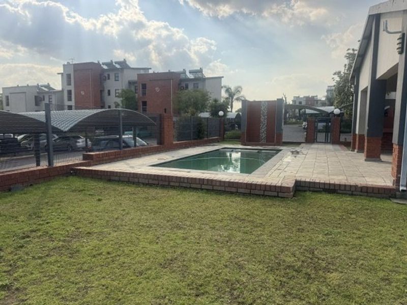 Outdoor pool area featuring a paved deck, brick boundary walls, and a lawn, situated within a residential apartment complex with adjacent carport parking.