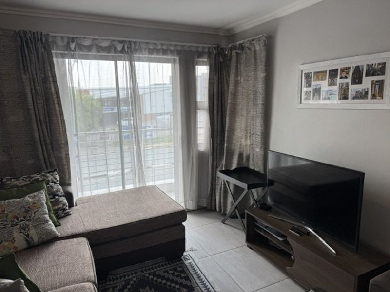 A living room featuring tiled flooring, neutral wall finishes, and a large sliding glass door providing natural light and access to the exterior.