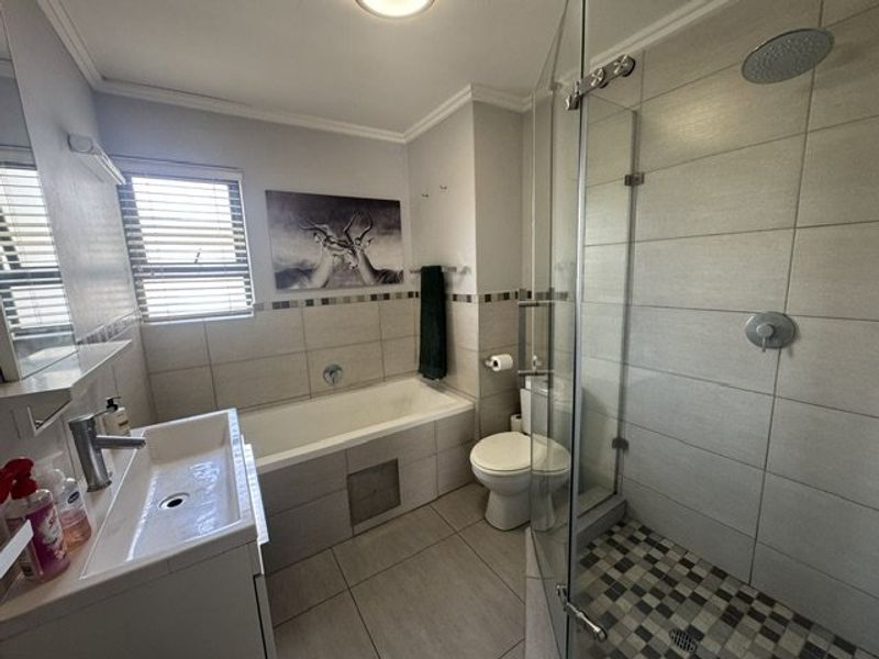 Modern bathroom featuring a glass-enclosed shower with rain head, a built-in bathtub, and a wall-mounted vanity basin with neutral tiled finishes.