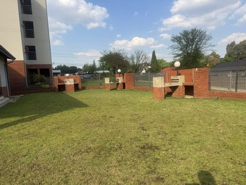 Communal garden area featuring multiple built-in brick braai stands and established lawn, situated within an apartment complex.