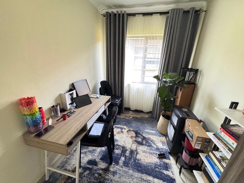 A compact home office space featuring neutral walls and a window with floor-to-ceiling curtains, providing a functional area for work or study.