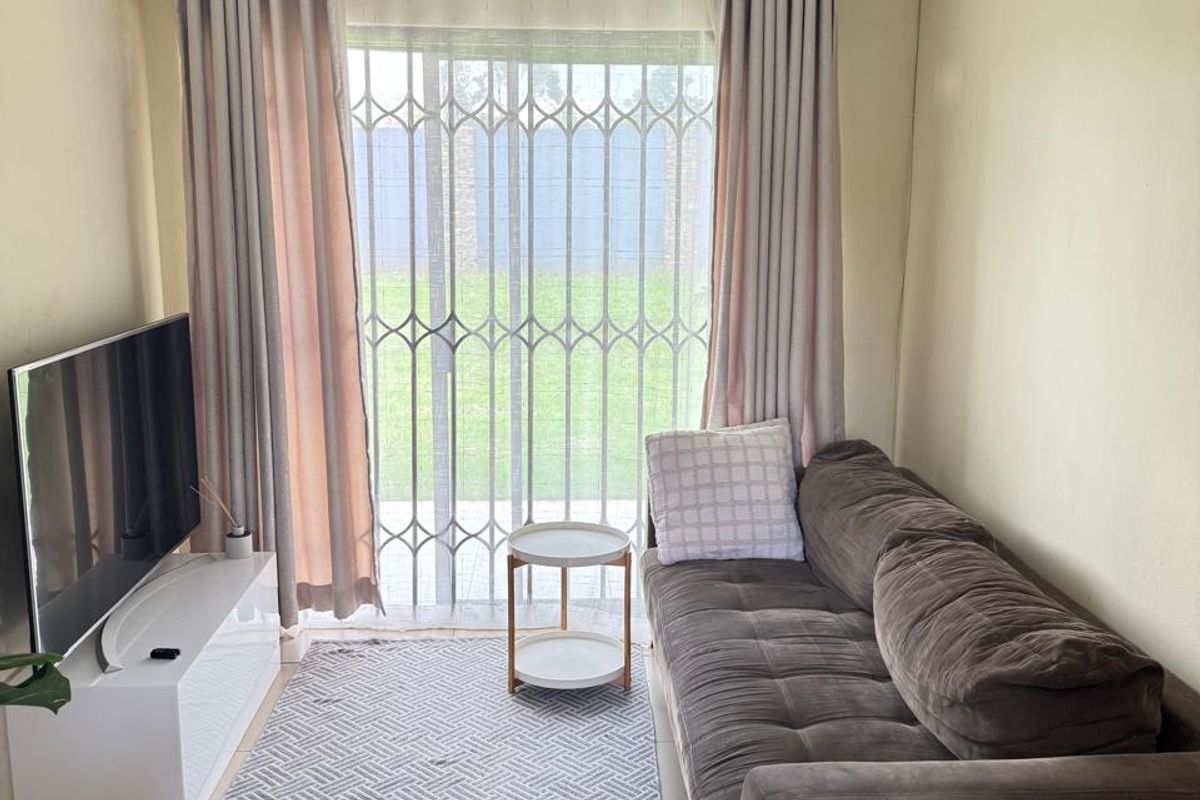A compact living room featuring tiled flooring, a ceiling spotlight fixture, and a sliding glass door with a security gate leading to the garden.