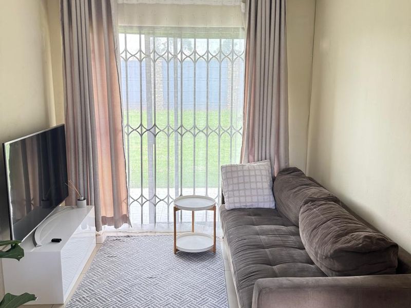 A compact living room featuring tiled flooring, a ceiling spotlight fixture, and a sliding glass door with a security gate leading to the garden.