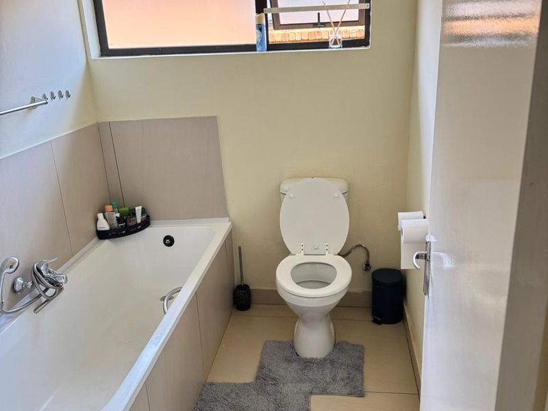 A functional bathroom featuring a bathtub with tiled splashback, a standard toilet, and tiled flooring, illuminated by a top-hung window.