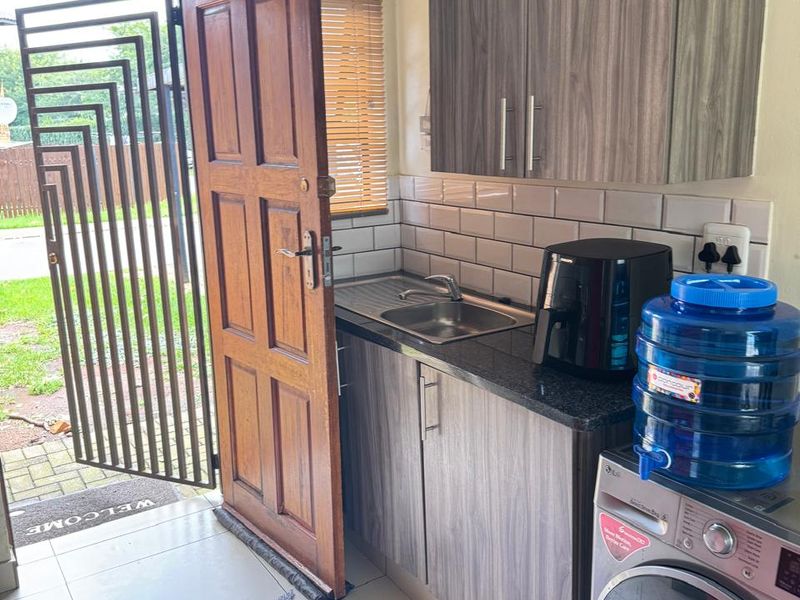 A functional scullery area featuring built-in cabinetry, a stainless steel sink, subway tile backsplash, and direct access to the exterior via a security gate.