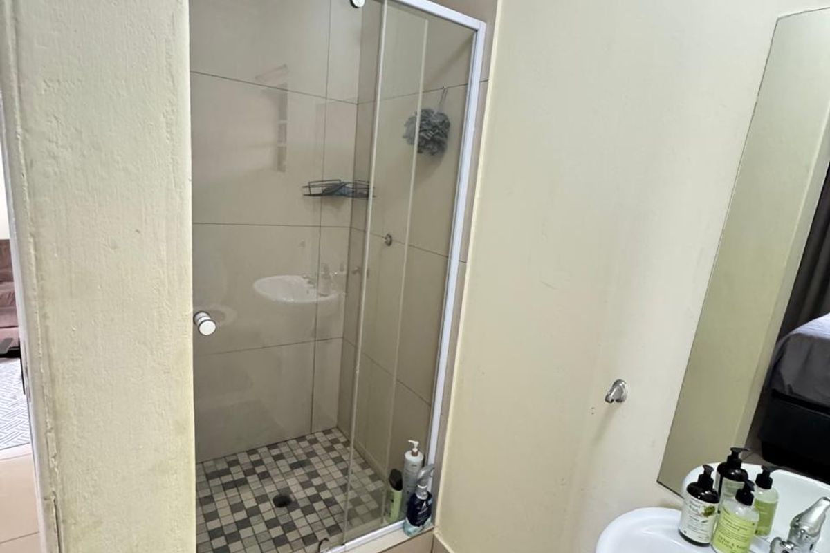 A functional bathroom featuring a glass-enclosed shower with tiled flooring and a pedestal basin, offering a clean and practical layout.