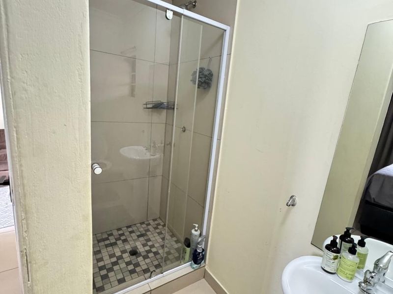 A functional bathroom featuring a glass-enclosed shower with tiled flooring and a pedestal basin, offering a clean and practical layout.