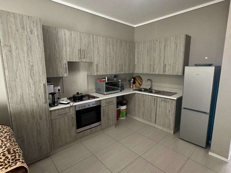 Modern kitchen featuring light wood-grain cabinetry, tiled flooring, integrated oven and hob, and ample counter space with a stainless steel sink.