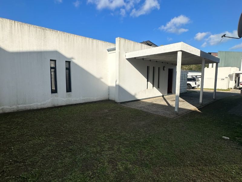 Front exterior view of the property featuring a covered carport, paved driveway, and a lawn area with white rendered walls.