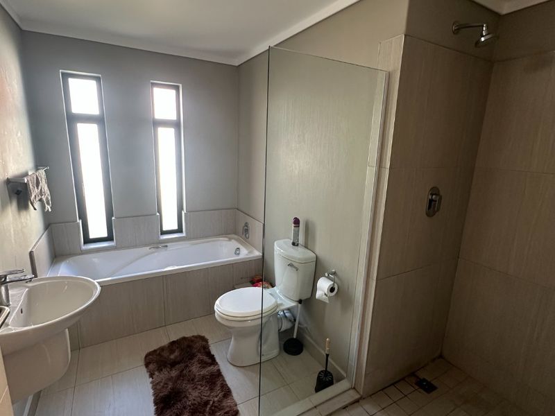 A modern bathroom featuring a built-in bathtub, a separate walk-in shower with a glass screen, a pedestal basin, and neutral floor-to-ceiling tiling.