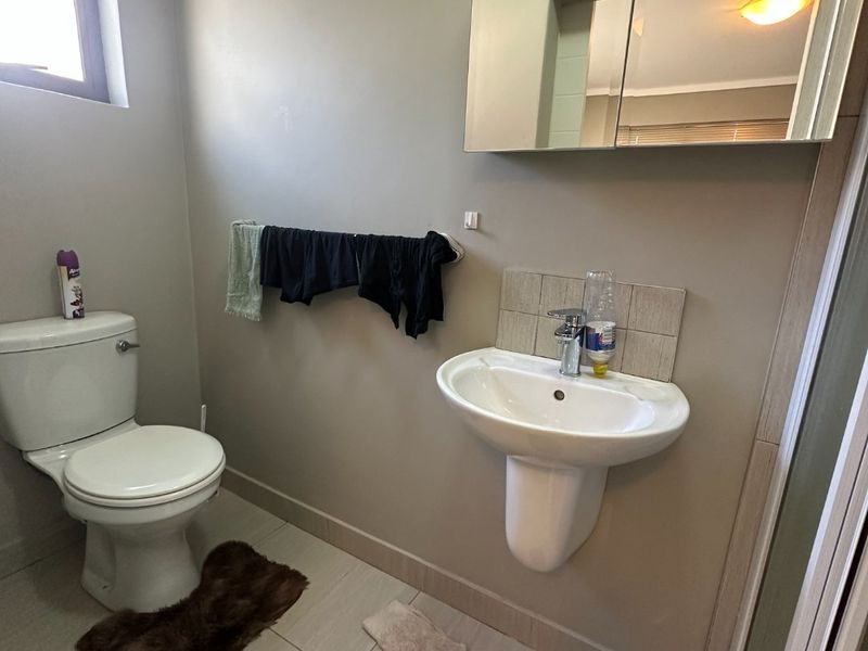 A functional bathroom featuring a pedestal washbasin, toilet, mirrored medicine cabinet, and a shower enclosure with neutral tiled flooring.