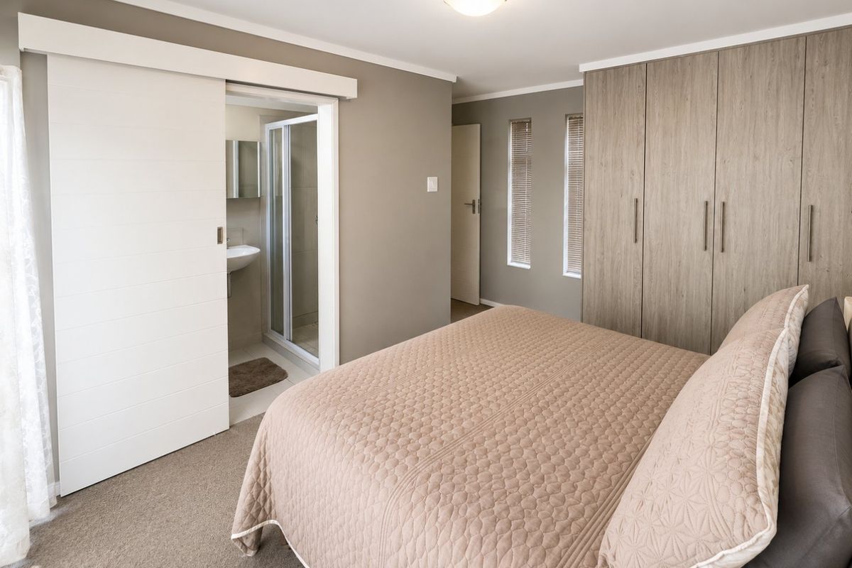 A well-maintained bedroom featuring built-in cupboards, carpeted flooring, and an en-suite bathroom with a shower and basin.