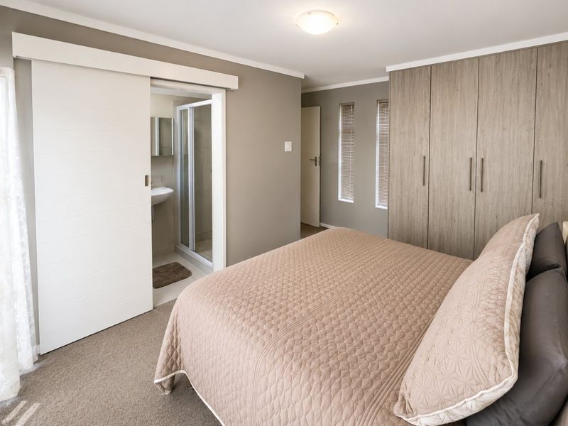 A well-maintained bedroom featuring built-in cupboards, carpeted flooring, and an en-suite bathroom with a shower and basin.
