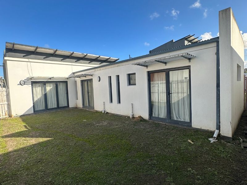 Rear view of the property featuring a lawn area, multiple sliding glass doors, and metal awnings over the entrances.