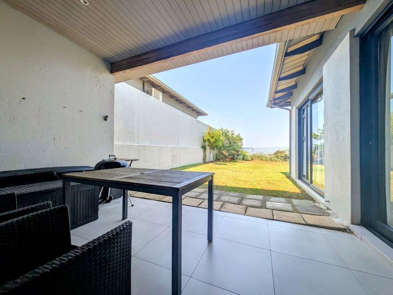 A covered patio area featuring tiled flooring and an exposed timber beam, providing seamless access to the rear garden through large sliding glass doors.
