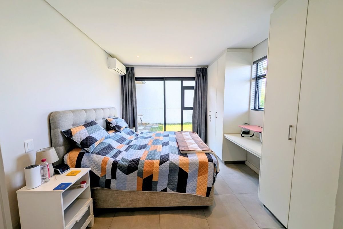 Modern bedroom featuring tiled floors, built-in cupboards, a built-in desk, split-system air conditioning, and direct access to the outdoor area via sliding glass doors.
