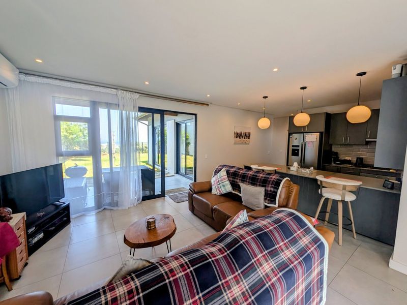 Modern open-plan living area featuring tiled floors, recessed lighting, and a contemporary kitchen with an island, seamlessly connecting to the outdoor patio.
