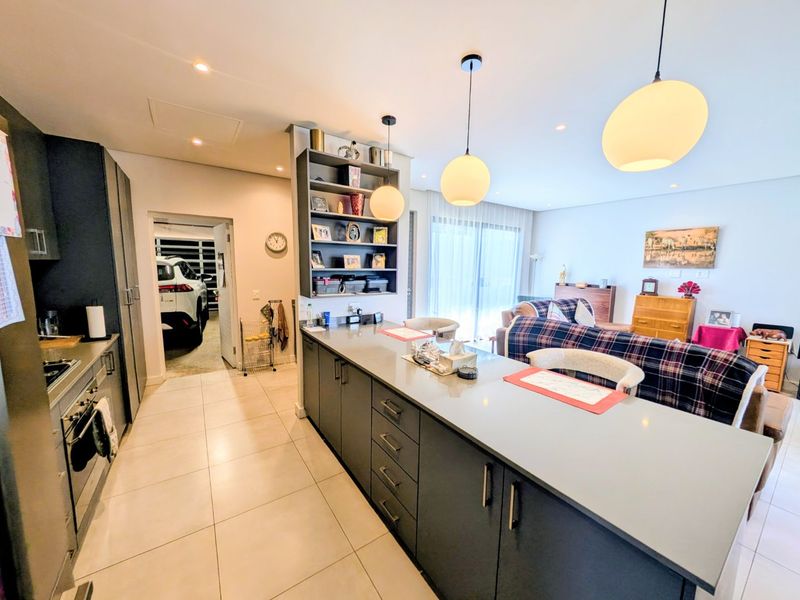 Modern open-plan kitchen and living area featuring a large central island, sleek cabinetry, stone countertops, and contemporary pendant lighting with direct access to the patio.