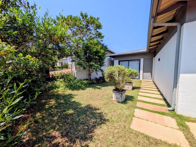 A well-maintained rear garden area featuring a paved walkway leading to a sliding glass door entrance, complemented by established greenery.