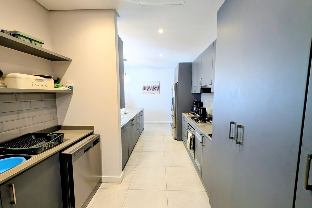 Modern galley-style kitchen featuring sleek grey cabinetry, stone countertops, integrated appliances, and a clean subway tile backsplash with ample storage space.