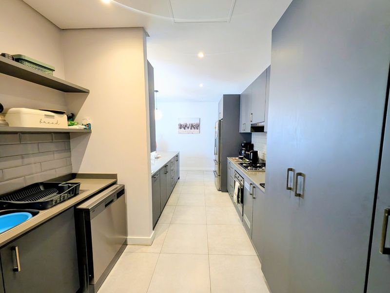 Modern galley-style kitchen featuring sleek grey cabinetry, stone countertops, integrated appliances, and a clean subway tile backsplash with ample storage space.