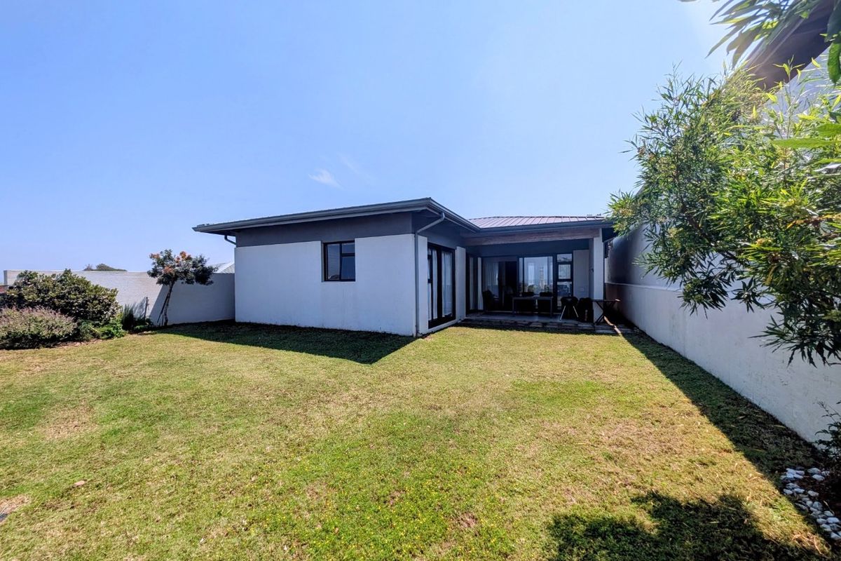 Rear view of the property featuring a well-maintained lawn, a covered patio area, and modern sliding glass doors leading into the home.