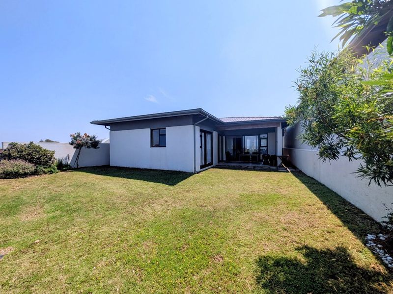 Rear view of the property featuring a well-maintained lawn, a covered patio area, and modern sliding glass doors leading into the home.
