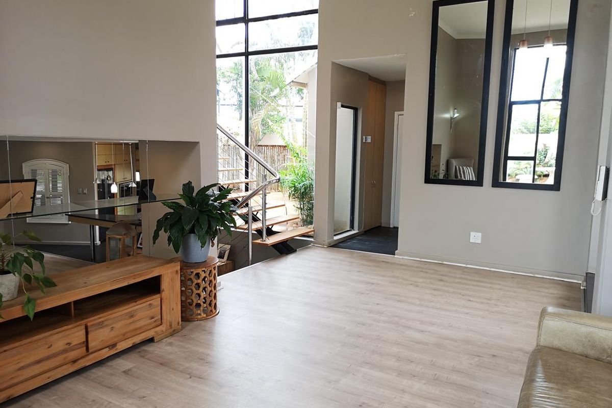 Spacious living area featuring modern laminate flooring, high ceilings, and a striking staircase with stainless steel railings, complemented by large windows for natural light.