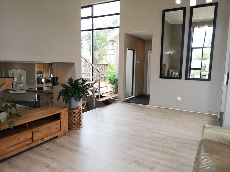 Spacious living area featuring modern laminate flooring, high ceilings, and a striking staircase with stainless steel railings, complemented by large windows for natural light.