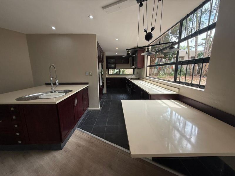 Spacious kitchen featuring dark wood cabinetry, stone countertops, a central island with sink, and large windows overlooking the garden.