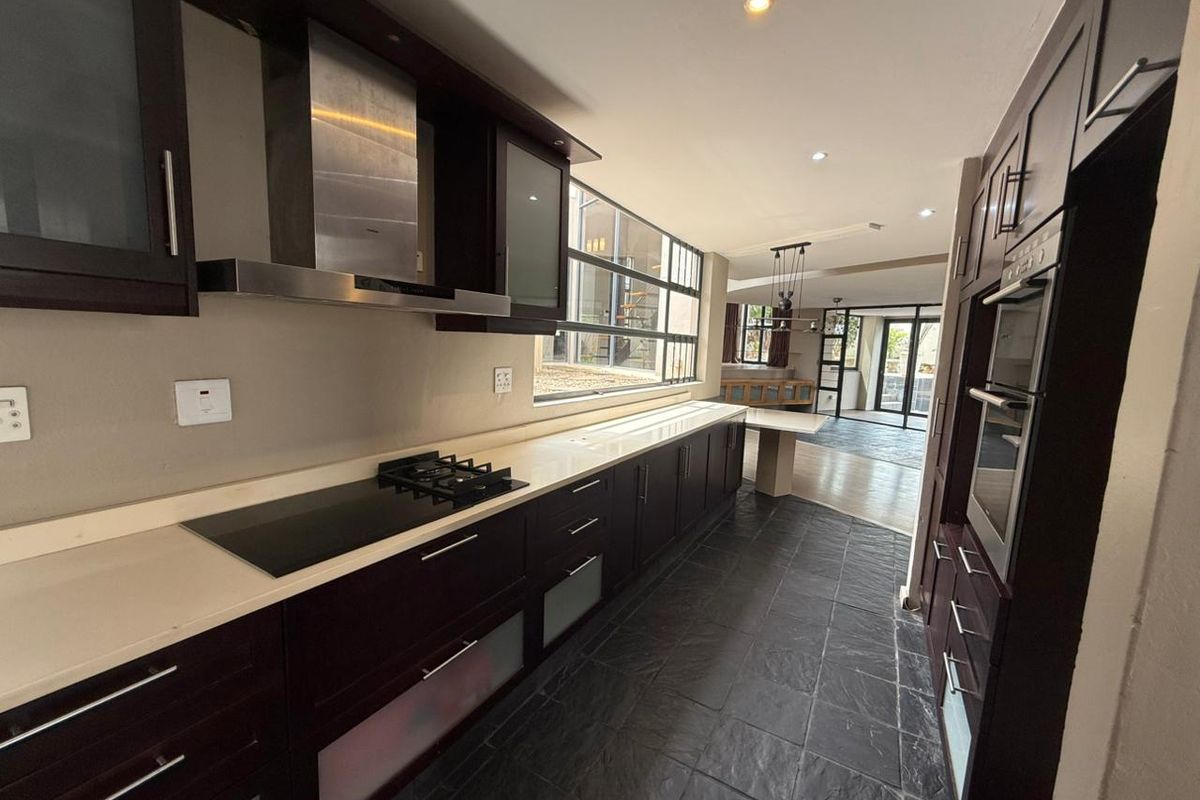 Modern kitchen featuring dark wood cabinetry, stone countertops, integrated appliances including a gas hob and oven, and slate tile flooring.