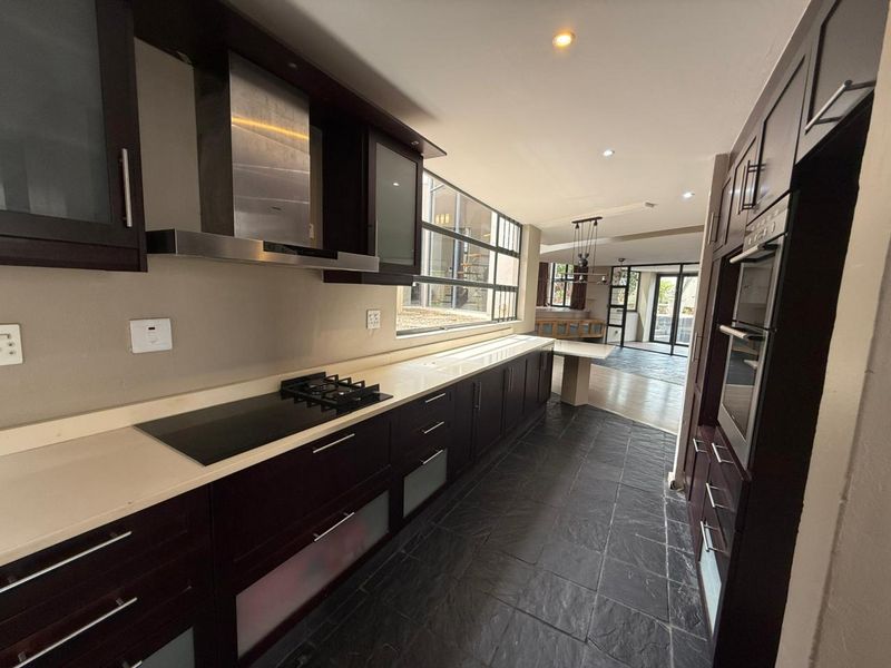 Modern kitchen featuring dark wood cabinetry, stone countertops, integrated appliances including a gas hob and oven, and slate tile flooring.