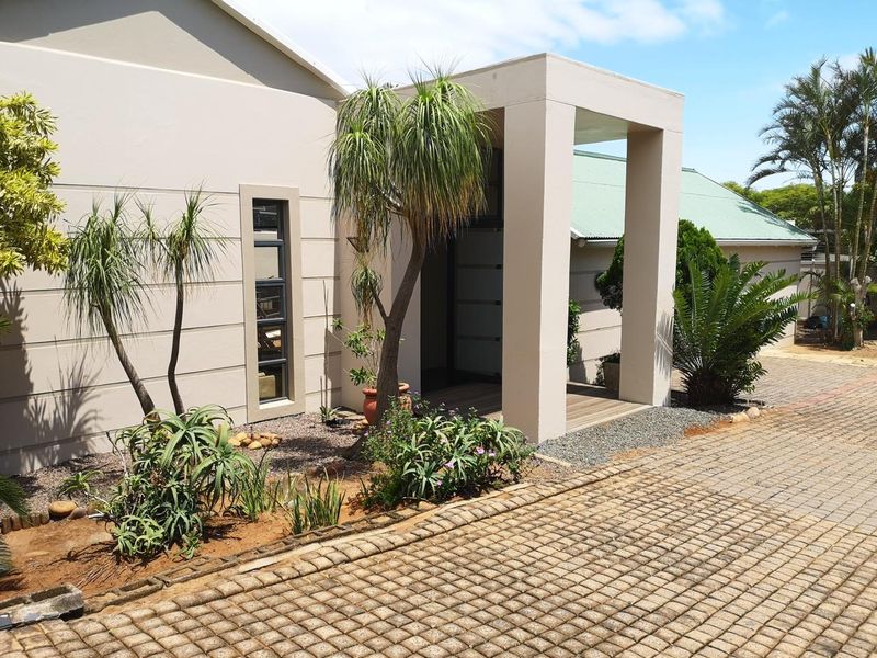 A modern front entrance featuring a paved driveway, covered porch with timber decking, and well-maintained landscaped garden beds.