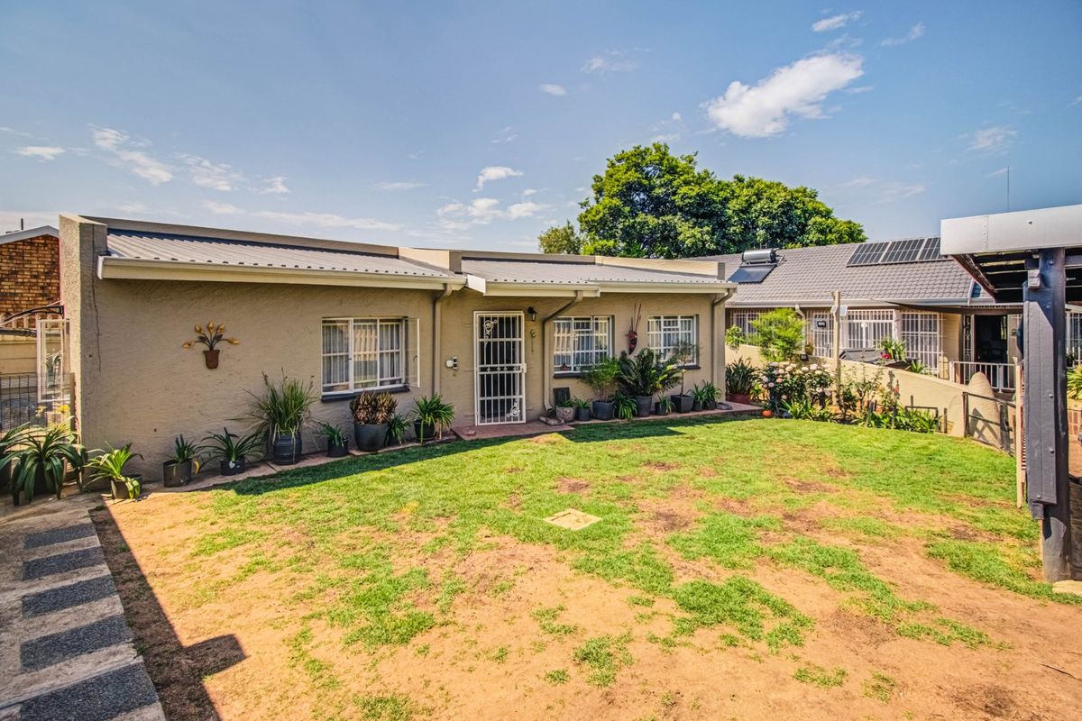 Rear view of the house featuring a metal roof, security gates, and a lawn area with established garden beds.
