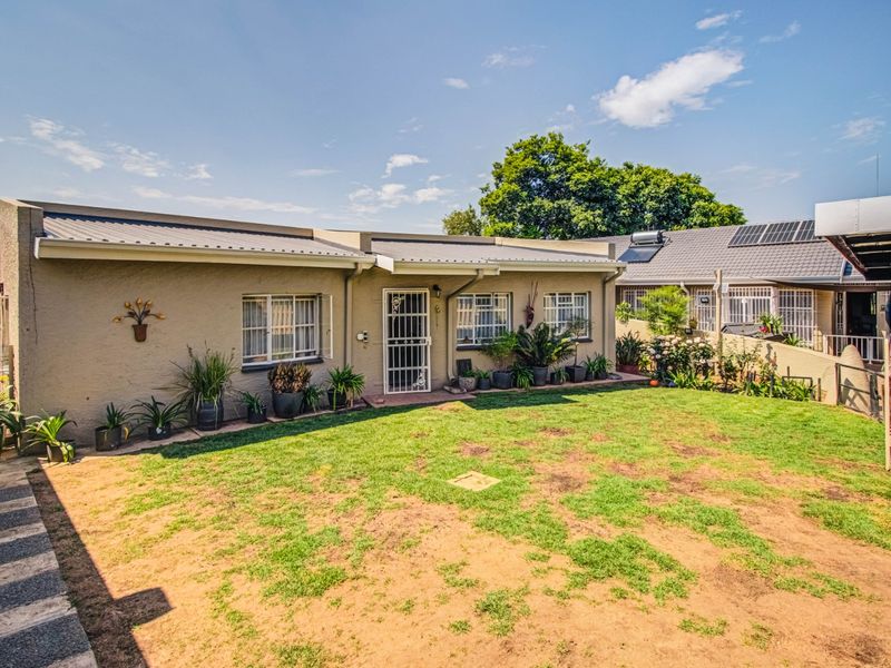 Rear view of the house featuring a metal roof, security gates, and a lawn area with established garden beds.