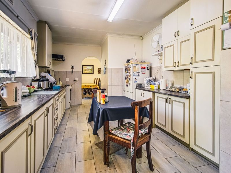 A functional kitchen featuring tiled flooring, ample built-in cabinetry, laminate countertops, and a tiled backsplash, leading through an archway to the dining area.