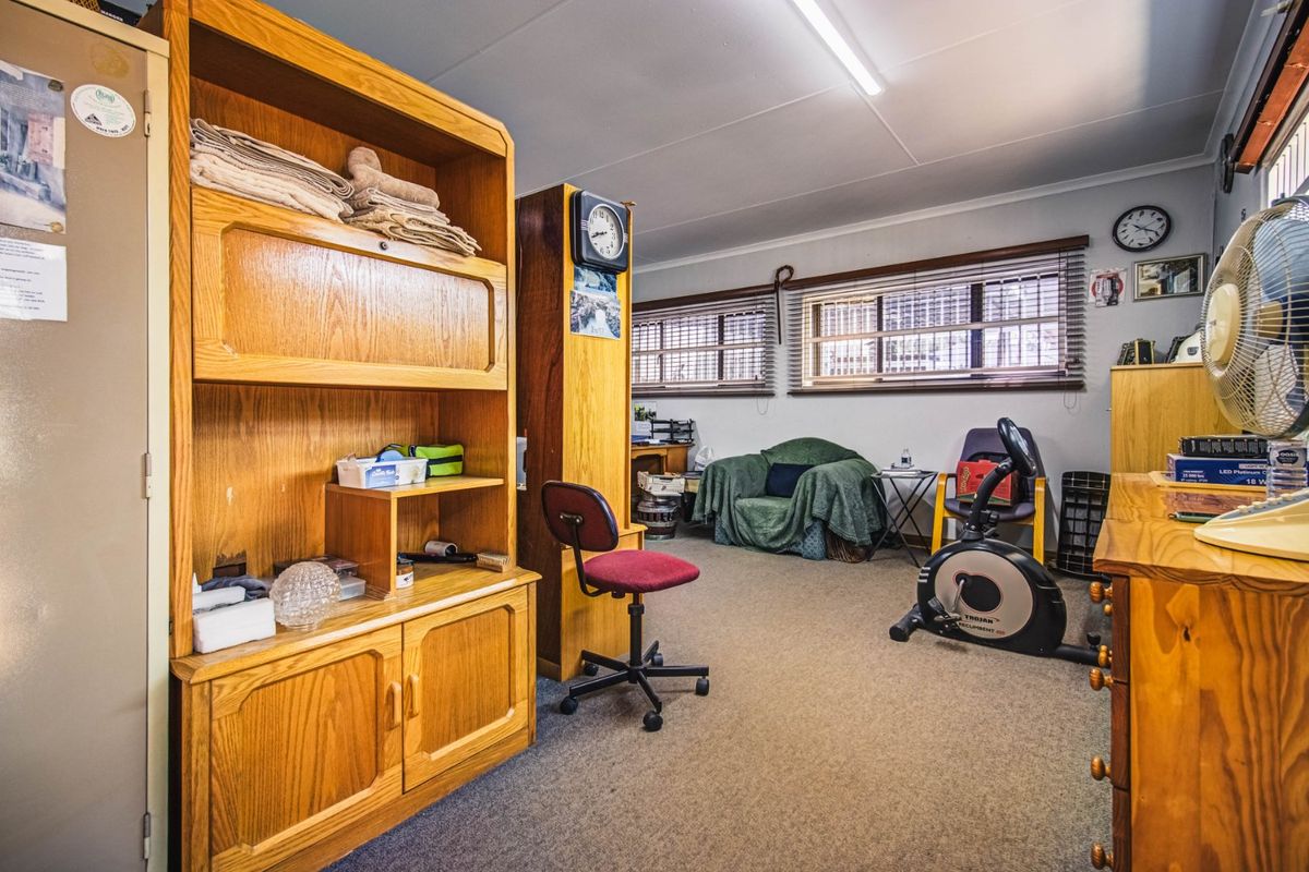 A multi-purpose room featuring carpet flooring, fluorescent lighting, and venetian blinds, currently utilized as a home office and exercise space.