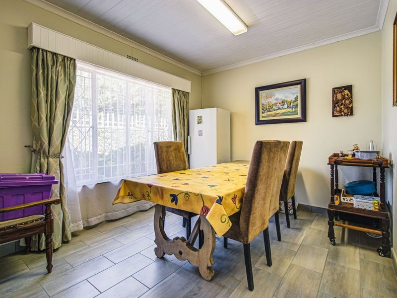 A dining room featuring tiled flooring, a tongue and groove ceiling, and a large window with security bars, providing a functional space for meals.