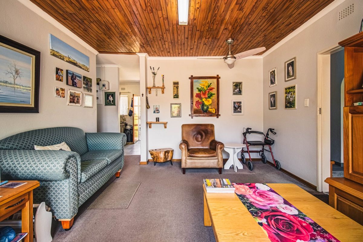 A comfortable living room featuring a warm timber tongue and groove ceiling, ceiling fan, and neutral carpeted flooring.