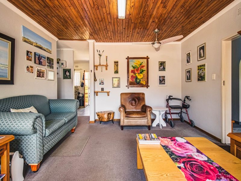 A comfortable living room featuring a warm timber tongue and groove ceiling, ceiling fan, and neutral carpeted flooring.