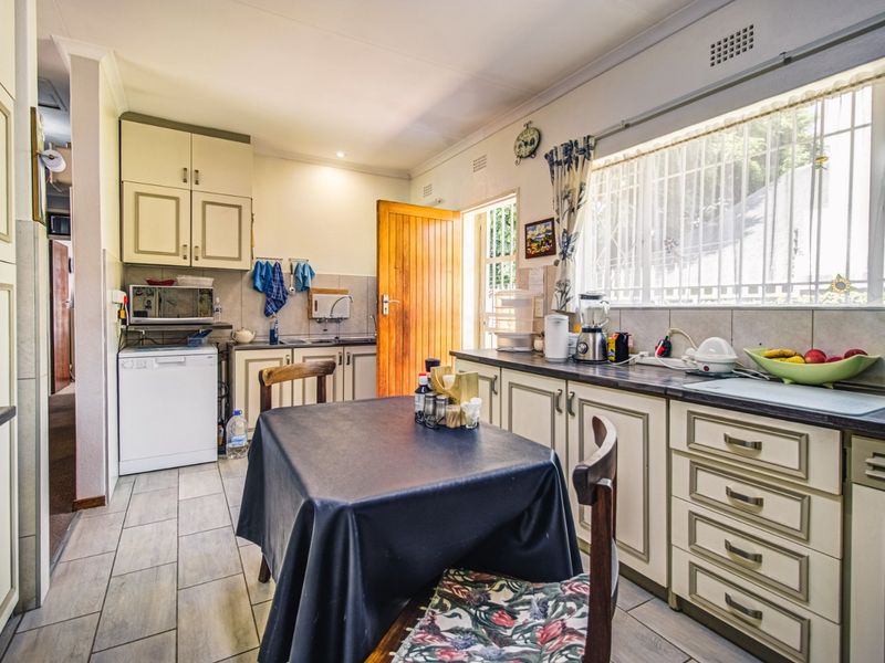A functional kitchen featuring built-in cabinetry, laminate countertops, and tiled flooring, with a window providing natural light and security bars.
