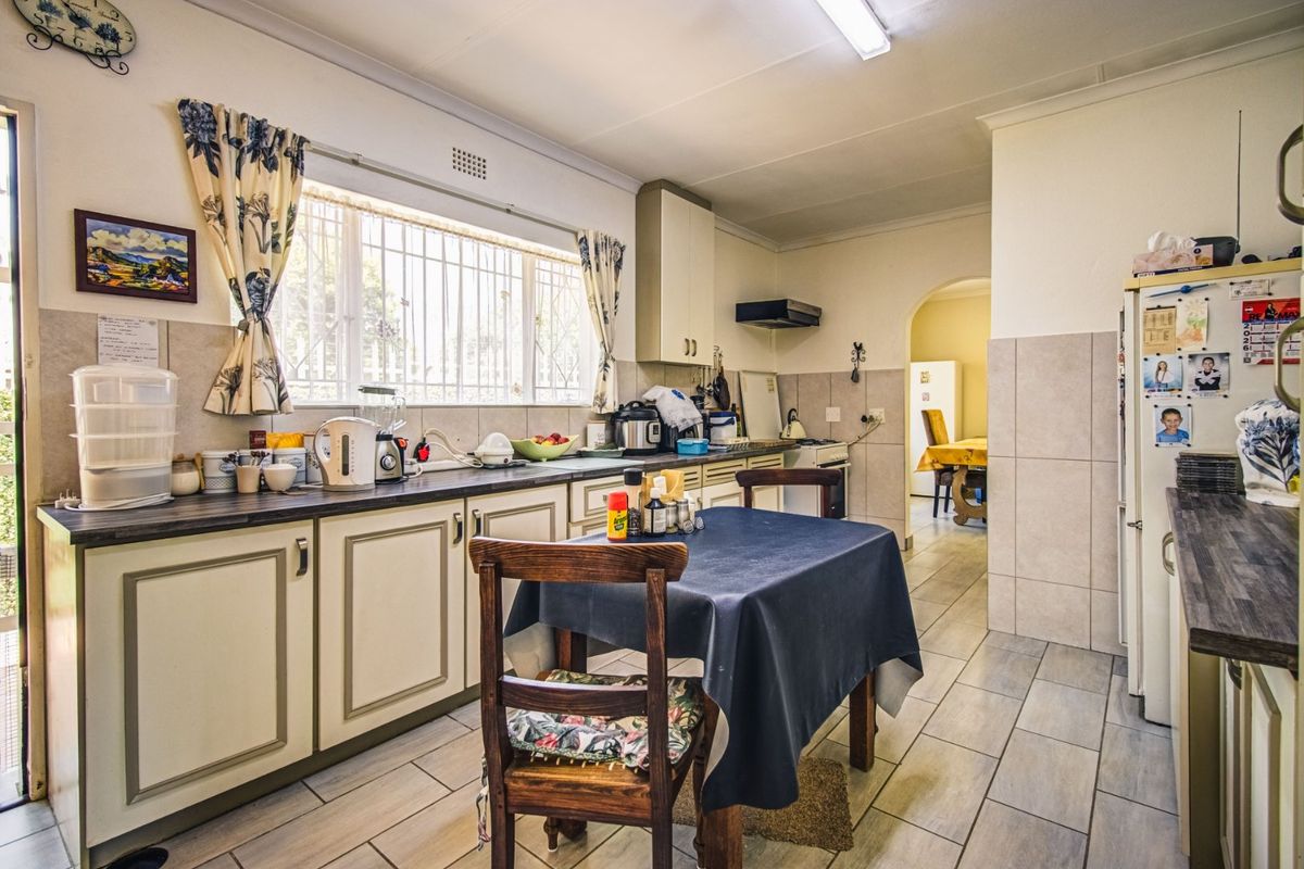 A functional kitchen featuring built-in cabinetry, laminate countertops, tiled backsplash, and tiled flooring, with an adjacent archway leading to a dining area.